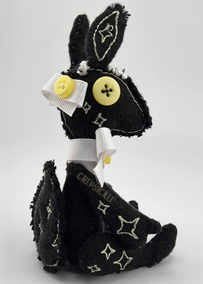 A black cotton plush creature with embroidered stars and button eyes