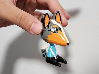 A hand holding a merle collie figure head between their thumb and pointer